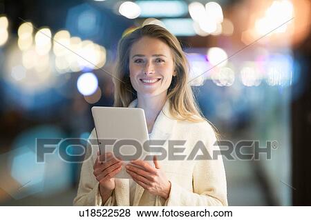 Stock Photo - Portrait of businesswoman using digital tablet on city street at night. Fotosearch