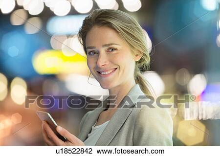 Stock Image - Portrait of businesswoman using smartphone on city street at night. Fotosearch