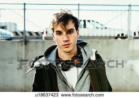 Stock Image - Portrait of man wearing hooded top and head phones looking at camera. Fotosearch