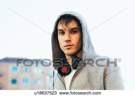 Stock Image - Portrait of man wearing hooded top and headphones looking at camera. Fotosearch