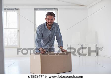 Stock Photo - Portrait of young man writing on cardboard box whilst moving house. Fotosearch