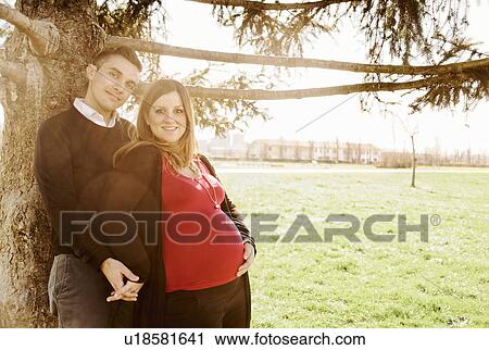 Pregnant couple leaning against tree in park View Large Photo Image Stock Image - Pregnant couple leaning against tree in park. Fotosearch