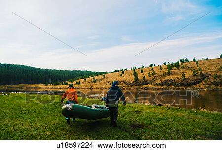 Picture - Rear view of couple carrying dinghy to river. Fotosearch