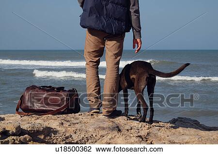 Rear waist down view of man and his dog on rocks by sea, Russia View Large Photo Image Stock Image - Rear waist down view of man and his dog on rocks by sea, Russia. Fotosearch