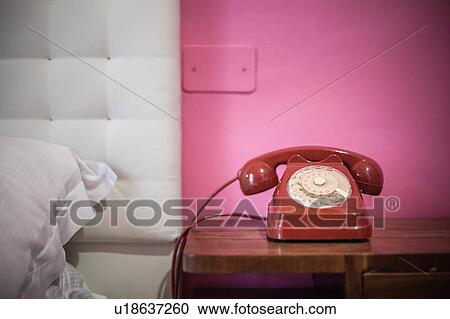 Stock Image - Red rotary telephone on bedside table. Fotosearch