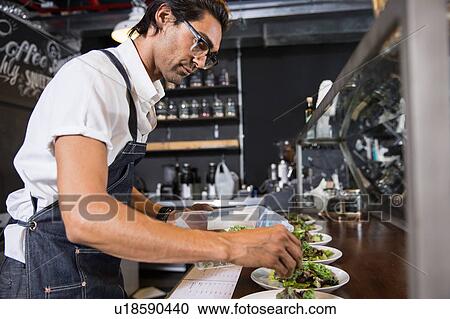 Stock Image - Restaurateur preparing salad behind service counter. Fotosearch