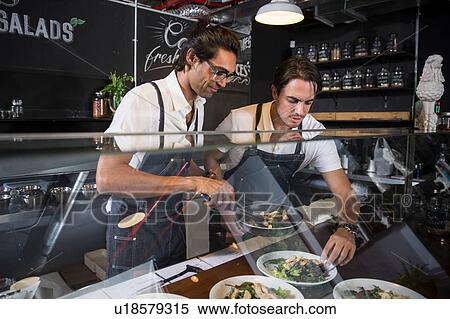 Restaurateurs preparing salad behind service counter View Large Photo Image Stock Photography - Restaurateurs preparing salad behind service counter. Fotosearch