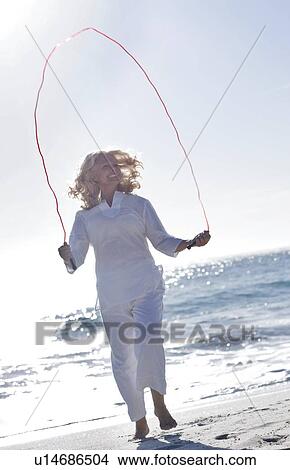 Picture - Senior woman skipping on a beach. Fotosearch