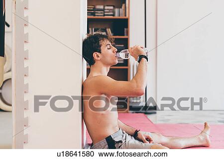 Stock Image - Side view of man leaning against column drinking water from bottle. Fotosearch