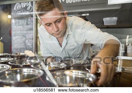 View through glass of restaurant worker arranging bowls in display cabinet View Large Photo Image Stock Image - View through glass of restaurant worker arranging bowls in display cabinet. Fotosearch
