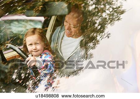 Stock Photo - View through windscreen of daughter sitting on father lap driving car. Fotosearch