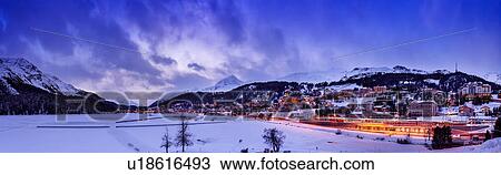 Stock Image - Village beneath mountain on snow covered landscape illuminated in the evening, Sankt Moritz, Switzerland. Fotosearch