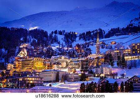 Stock Photo - Village beneath mountain on snow covered landscape illuminated in the evening, Sankt Moritz, Switzerland. Fotosearch