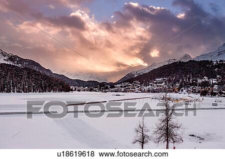 Stock Photo - Village beneath mountain on snow covered landscape at sunset, Sankt Moritz, Switzerland. Fotosearch