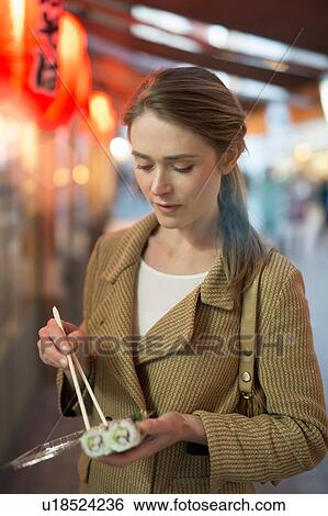 Woman eating takeaway sushi on city street at night View Large Photo Image Stock Photograph - Woman eating takeaway sushi on city street at night. Fotosearch