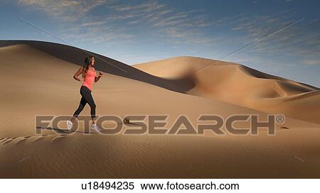Stock Photography - Woman jogging on desert sand dune, Empty Quarter Desert, Abu Dhabi, United Arab Emirates. Fotosearch