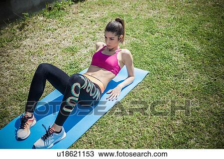 Stock Image - Woman on grass on exercise mat doing sit ups. Fotosearch