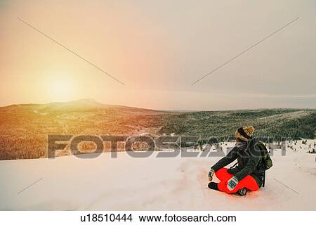 Picture - Woman on snow covered landscape sitting looking at view of sunset over mountain. Fotosearch