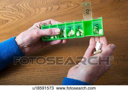 Stock Image - Woman taking medication out of pill box. Fotosearch