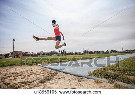 Stock Photography - Young female long jumper jumping mid air at sport facility. Fotosearch