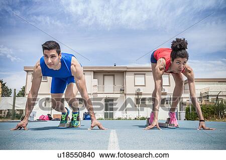 Stock Image - Young male and female sprinters on their marks on running track. Fotosearch