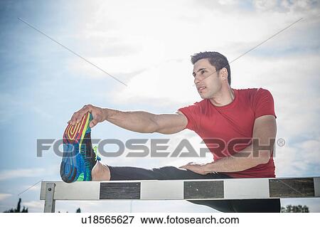 Stock Photo - Young male hurdler warming up on sport hurdle. Fotosearch