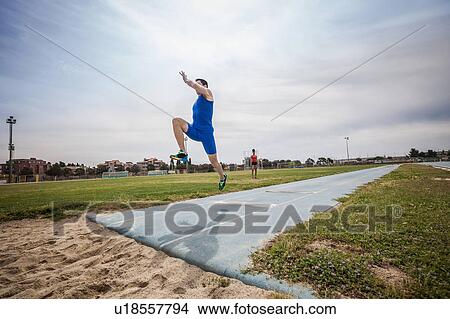 Picture - Young male long jumper jumping mid air at sport facility. Fotosearch