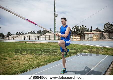 Stock Photograph - Young male pole vaulter pole vaulting at sport facility. Fotosearch