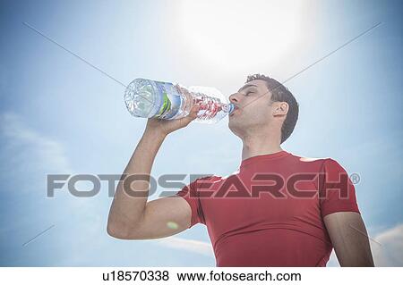 Young man drinking bottled water against blue sky View Large Photo Image Stock Photo - Young man drinking bottled water against blue sky. Fotosearch
