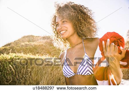 Stock Photo - Young woman on sand dune carrying beach towel, Cape Town, South Africa. Fotosearch
