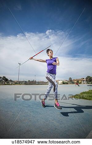Stock Photo - Young woman throwing javelin in sports ground. Fotosearch