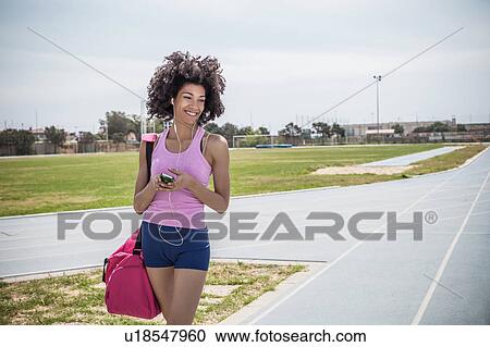 Stock Image - Young woman training, listening to earphones on running track. Fotosearch