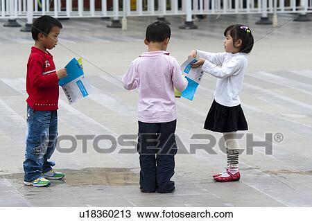 Stock Image - Boys and girl playing with magazines, Shanghai, China. Fotosearch