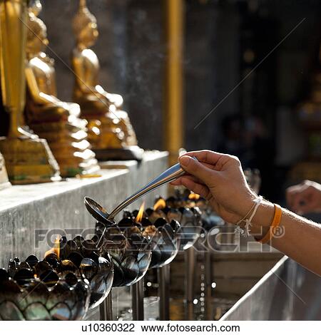 Stock Image - Close-up of a person's hand pouring oil into an oil lamp at Wat Phrathat Doi Suthep, Chiang Mai, Thailand. Fotosearch