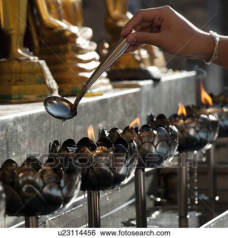 Stock Photograph - Close-up of a person's hand pouring oil into an oil lamp at Wat Phrathat Doi Suthep, Chiang Mai, Thailand. Fotosearch