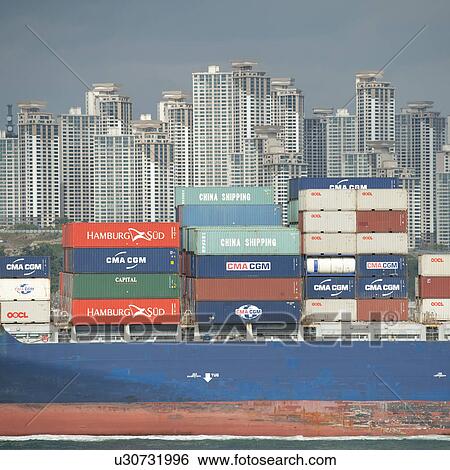 Stock Photograph - Container ship with city skyline in the background at Busan harbor, Busan, Yeongnam, South Korea. Fotosearch
