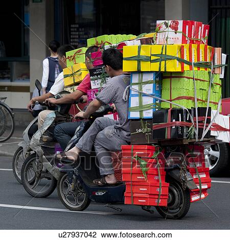 Stock Image - Men carrying cardboard boxes on mopeds, Shanghai, China. Fotosearch
