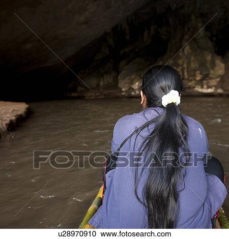 Stock Image - Rear view of a woman sitting on a bamboo boat, Thailand. Fotosearch