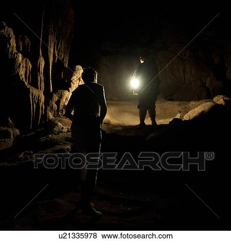 Stock Photo - Tourists in a dark cave with a lantern, Thailand. Fotosearch