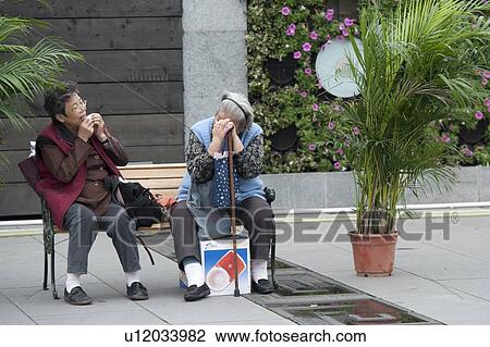 Stock Image - Two women sitting on a bench, Shanghai, China. Fotosearch