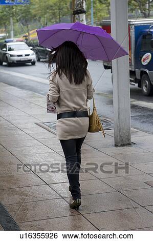 Stock Photograph - Woman holding an umbrella and walking on a footpath, Shanghai, China. Fotosearch