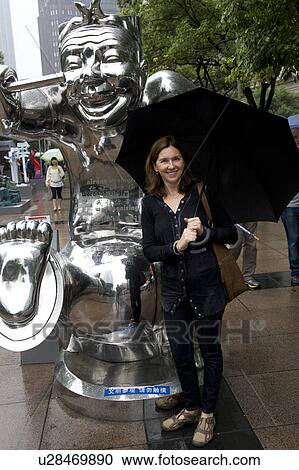 Stock Image - Woman standing beside a statue, Shanghai, China. Fotosearch