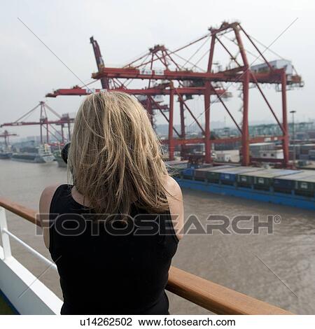 Stock Image - Woman taking picture of commercial dock, Yangtze River, Shanghai, China. Fotosearch