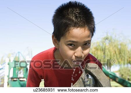 Stock Image - Boy (12-13) at drinking fountain. Fotosearch