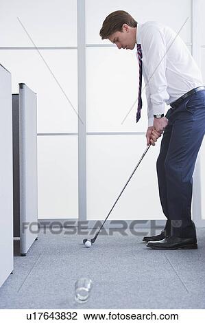 Stock Image - Businessman playing golf at office. Fotosearch
