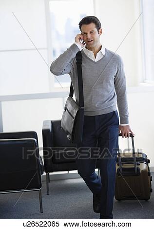 Businessman pulling suitcase and talking on mobile phone in airport lounge View Large Photo Image Stock Photography - Businessman pulling suitcase and talking on mobile phone in airport lounge. Fotosearch