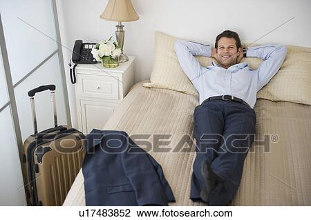 Businessman relaxing on bed in hotel room View Large Photo Image Stock Image - Businessman relaxing on bed in hotel room. Fotosearch