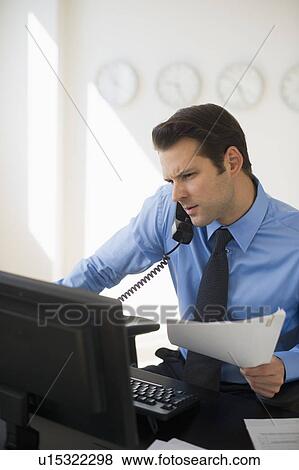 Stock Photo - Businessman working on computer and talking on the phone. Fotosearch