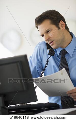 Stock Photo - Businessman working on computer and talking on the phone. Fotosearch