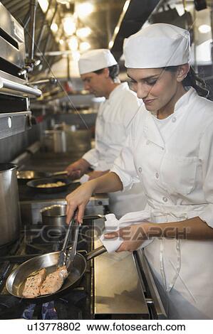 Stock Image - Chef and cook preparing food in commercial kitchen. Fotosearch